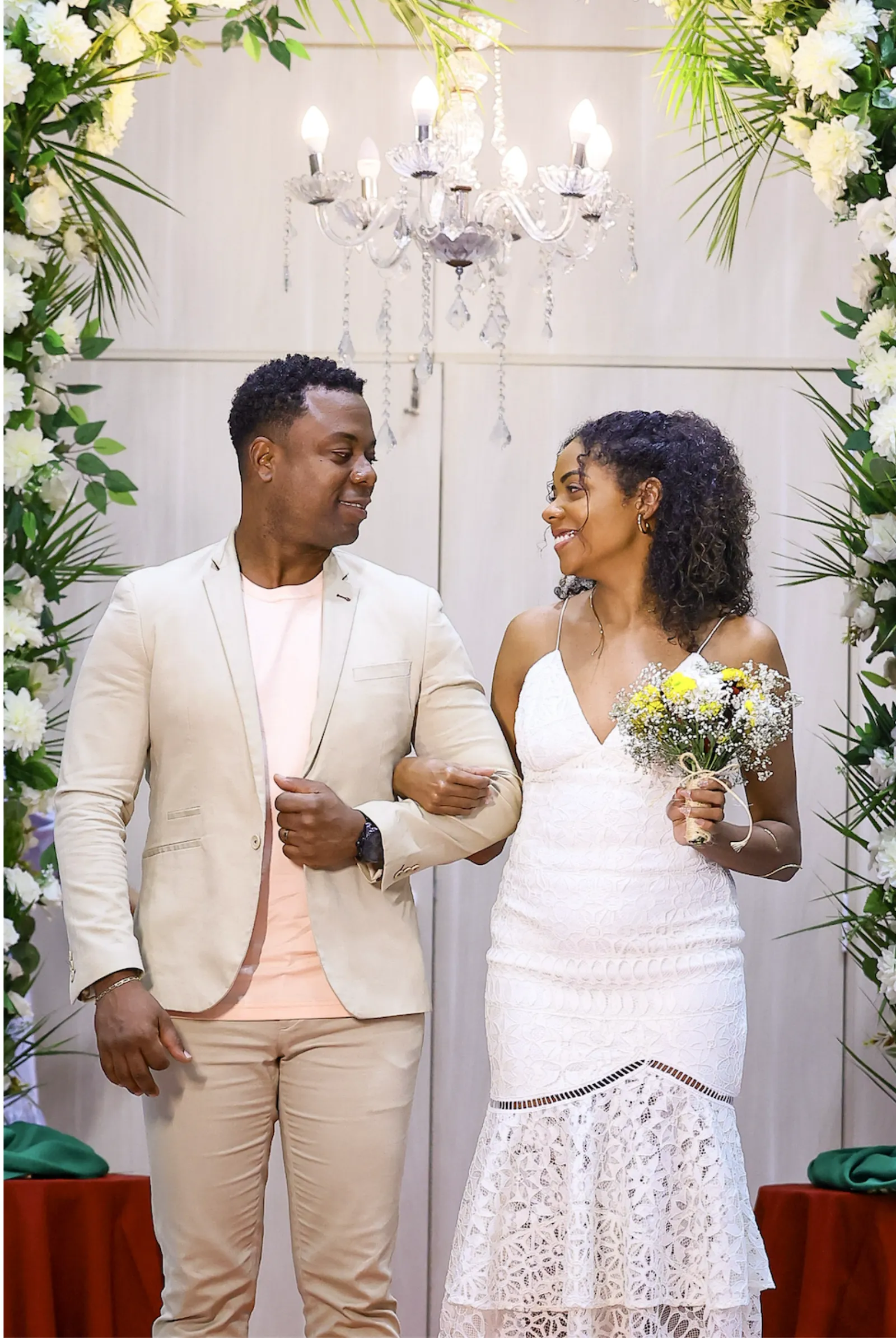 Casal renovando votos sob arco floral e lustre de cristal no RC2