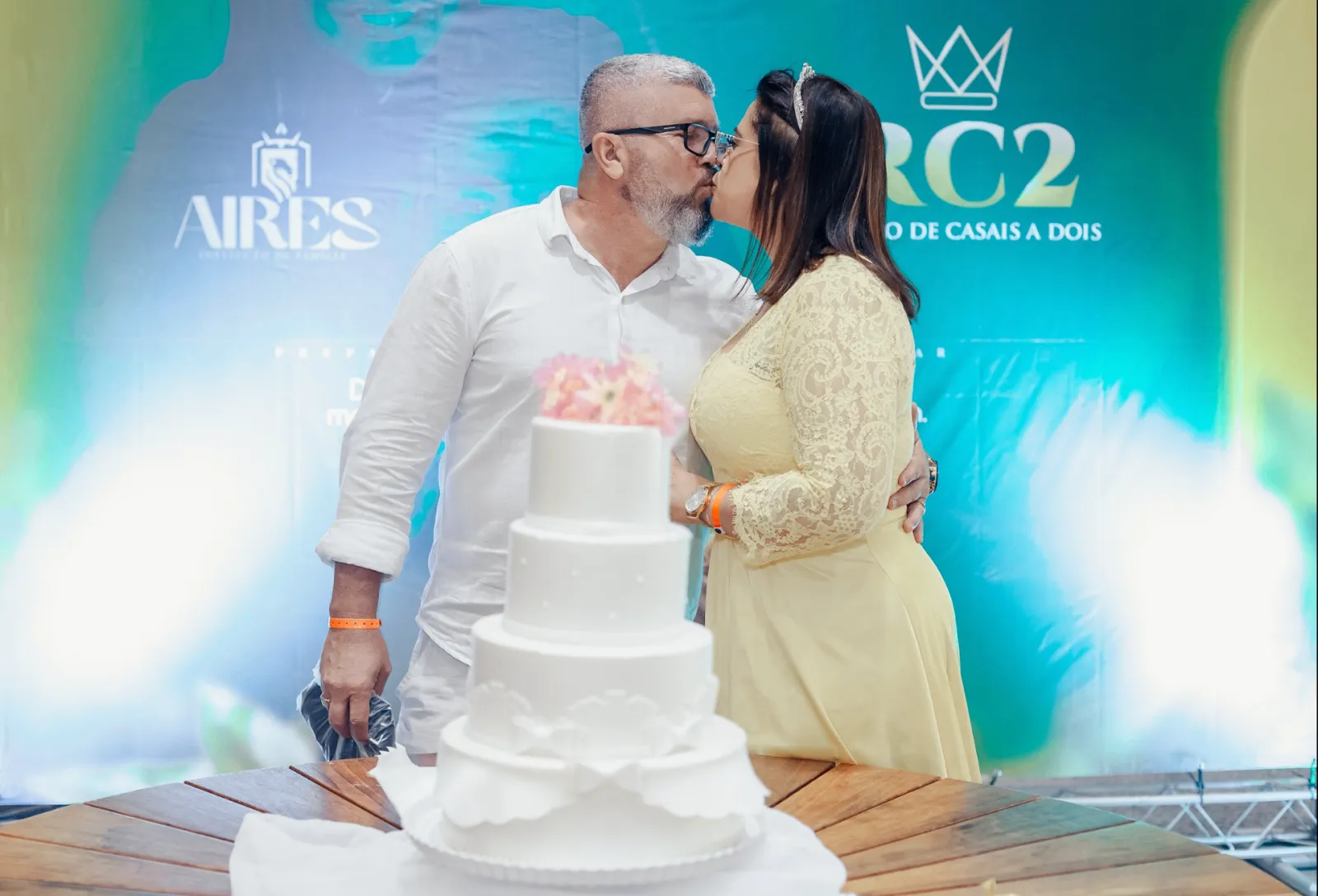 Casal celebrando renovação de votos com beijo e bolo no palco do RC2